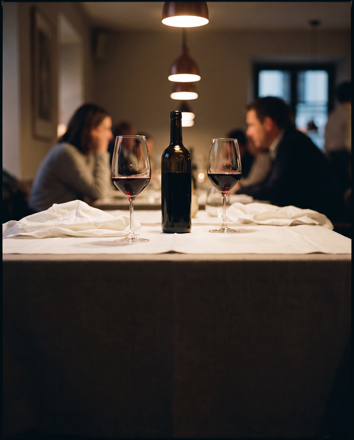 Gedekte restauranttafel met rode wijn onder een warme hanglamp